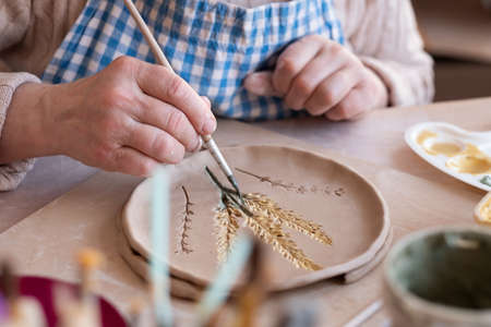 Senior female artist making flower ornament on ceramic product.の写真素材