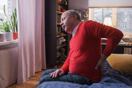 Senior man suffering from pain in back or reins at home