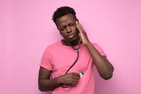 African man listening to his heart with stethoscope isolated on pink background. Preventive medicine, financial condition check up conceptの写真素材