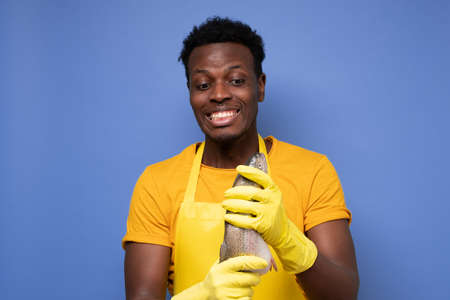 African young cook holding a fresh fish on a purple background. studio shotの写真素材