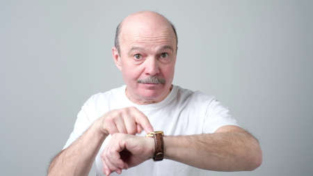 Mature man showing time on his watch saying you are late, being annoyed.の写真素材