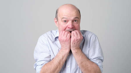 Portrait of anxious senior man biting his nails fingers freaking out. I am afraid that I will be exposed and someone will know my terrible secret emotionの写真素材