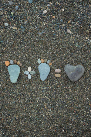 concept of family. Steps of man, woman and heart made from stones on sandy beach.の写真素材