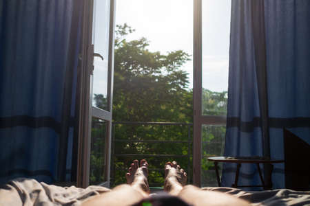 Man legs lying on bed. view on window. It is hot inside without air condition.の写真素材