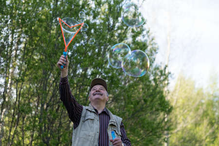 Senior active man plays with soap bubbles outdoor remembering childhoodの写真素材