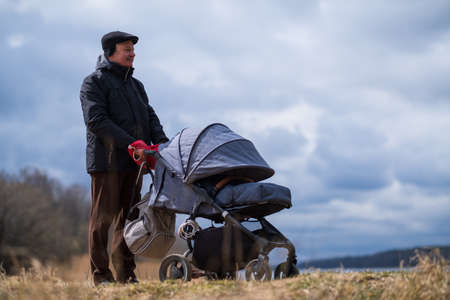 Grandfather walking with a baby stroller on spring day on natureの写真素材