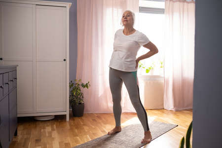 Happy senior lady doing yoga asana at living room.