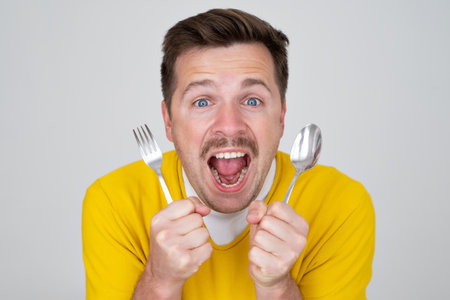 handsome hungry young man holding fork and spoon waiting for dinnerの写真素材