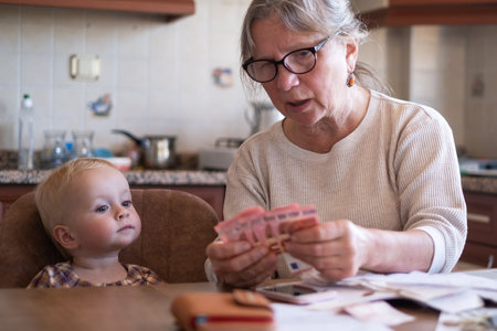 Senior woman counting money americain dollars and euro at home teaching kidの写真素材