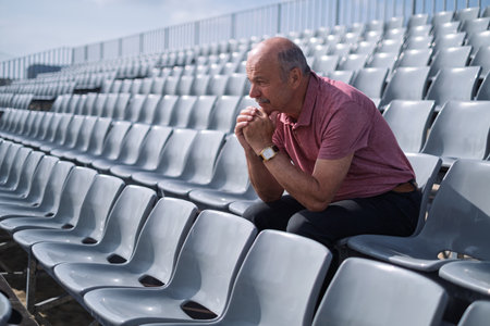 Elderly Spanish Man Sitting Alone on Stadium Stands Feeling Sadの写真素材