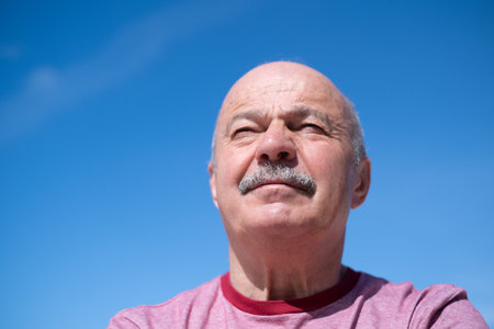 Elderly Spanish Man Against Blue Sky, Slightly Sad and Frowningの写真素材