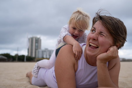 Woman in sportswear relaxing on the beach with her daughter on the sand.の写真素材