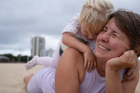 Woman in sportswear relaxing on the beach with her daughter on the sand.の写真素材