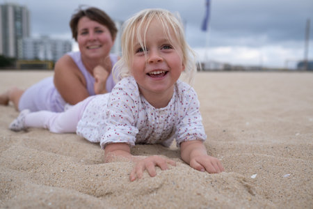 Woman in sportswear relaxing on the beach with her daughter on the sand.の写真素材