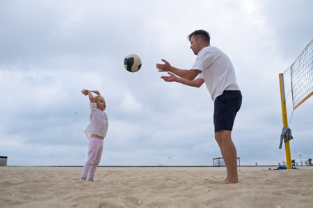 Father teaching his 4-year-old daughter to play beach volleyball.の写真素材