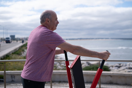 Elderly man exercising on outdoor fitness equipment by the ocean in Portugal, healthy lifestyleの写真素材
