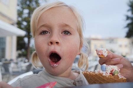 Girl eating ice cream and looking surprised at cameraの写真素材