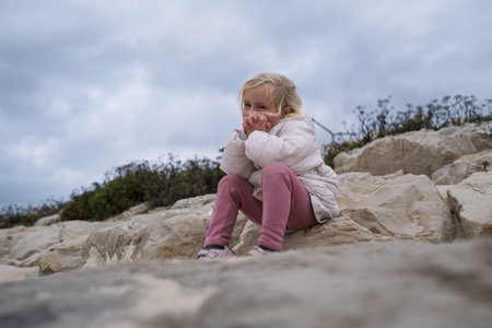 A young girl is sitting on the ocean shore and looking sadly at the sea,の写真素材