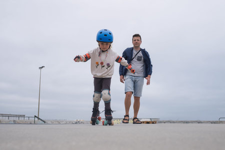 irst Steps on Wheels. Cute Little Girl Learning to Roller Skate with Supportive Father