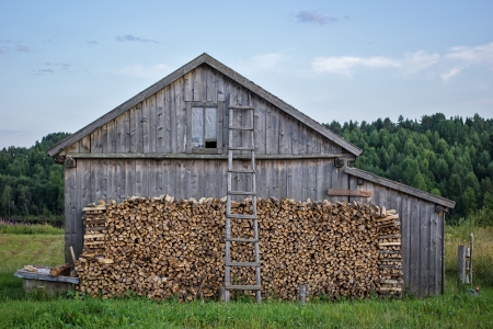 old wooden barn with firewood and a ladder on a background of forestのeditorial素材