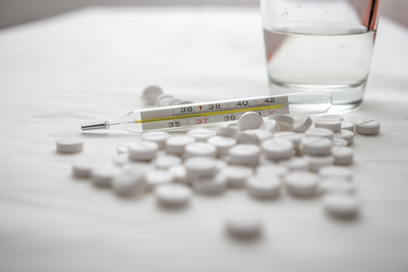 In medical thermometer temperature 37 degrees, and in the background are on the table white pills and glass of waterの写真素材