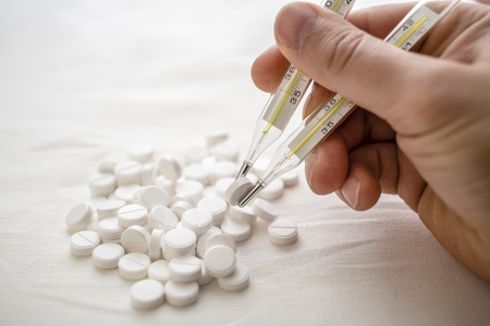 man is going to eat the drug tablets and holds two medical thermometer like chopsticksの写真素材