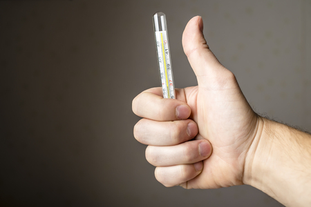 a sick man holding a medical thermometer and showing thumb indicating that he is all rightの写真素材