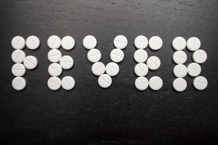 the word "fever" is made on a black table using white medicinal tabletsの写真素材