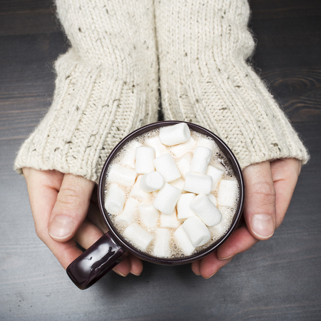 warming cup of cocoa with marshmallows in his hands during the cold winterの写真素材