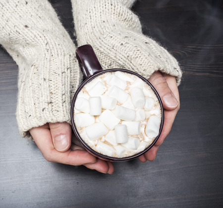 warming cup of cocoa with marshmallows in his hands during the cold winterの写真素材