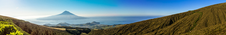 Long panorama of the beautiful landscape in the Azores at sunrise lonely island with a volcano hidden in the haze over the Atlantic Ocean.の写真素材