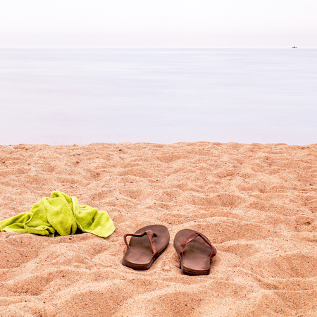 People sailed away in the sea and can be seen on the horizon, and slippers and a towel left on the sand on the beachの写真素材