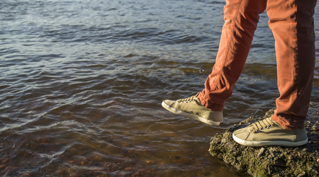 close-up of legs of a man who takes a step from stone into the river, summer eveningの写真素材