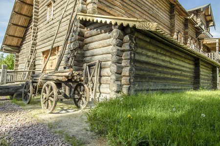 quaint, traditional Russian log house, in the yard on the green grass is a cart with logs on a sunny summer dayの写真素材