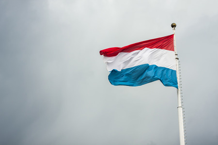 Luxembourg flag fluttering in the wind against the sky covered with clouds on a white flagpoleの写真素材