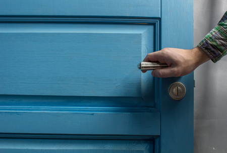 man holding on to by its metal handle in the open wooden door blueの写真素材