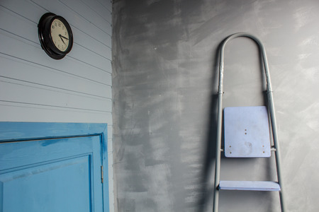 repair in an apartment by using a stepladder which stands leaning on wall by the door of blue color above which are hanging clockの写真素材