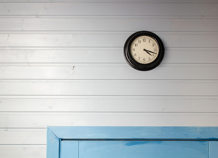 the round clock hanging on a wall lined with wooden siding is on the blue doorの写真素材