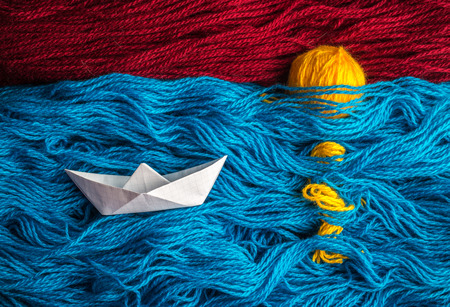 Cute white of origami boat floating on the waves of woolen yarn to the sunset, where are visible on a surface of rays of the sunの写真素材