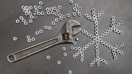 sign snowflake made up of screws nuts on a dark wooden table, next is adjustable wrench with the...
