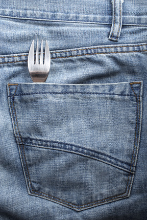 hungry man carries a fork into the back pocket of jeans for a snackの写真素材