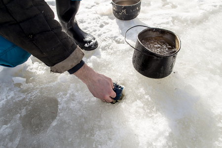 fisherman draws water from hole in the ice with the help of a cup, fill pots for cookingの写真素材
