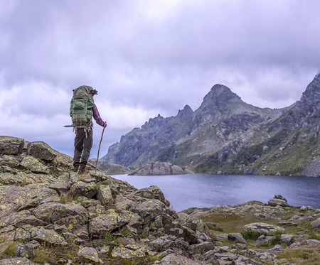 man with a backpack standing on vintage background of high mountains drowning in clouds and clear lakeの写真素材