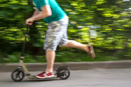 man rides a scooter at speed down the road, blurred background the green treesの写真素材