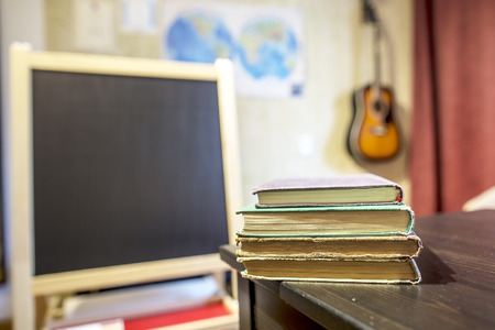 Books lying on a table in a classroom at a private school with a black board, card and guitar on the wallの写真素材