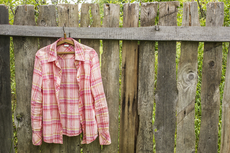 Shirt hangs a on hanger on the old fence of outdoors the boards in a villageの写真素材