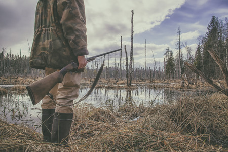 Hunter standing in the swamp in the forest and holding in his hand an old hunting rifleの写真素材