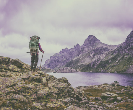 man with a backpack standing on vintage background of high mountains drowning in clouds and clear lakeの写真素材