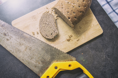hard stale bread and cut off a piece of it lie on a wooden cutting board, rusty hacksaw lying besideの写真素材