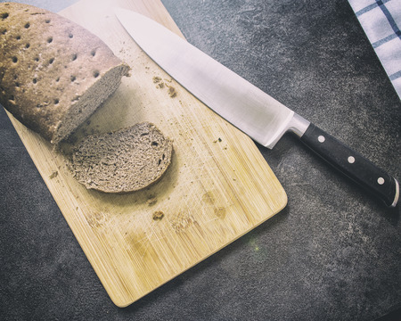 hard stale bread and cut off a piece of it lie on a wooden cutting board, knife lying besideの写真素材